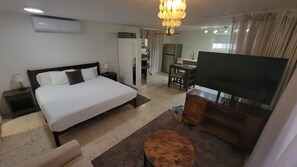 Ein Hotelzimmer mit Bett, Fernseher, Schreibtisch und einer Küchenzeile.