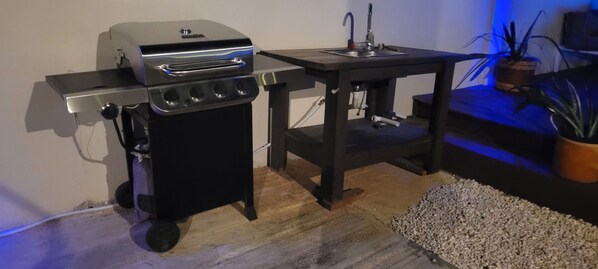 A compact kitchen setup with a portable grill, a sink, and a small table.