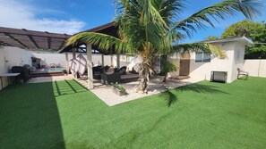 A backyard with artificial grass, a palm tree, outdoor furniture, and a pool.