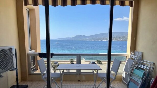 Un balcón con mesa y sillas, vista al mar y una playa en el fondo.