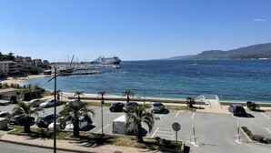 Un área de estacionamiento costero con vehículos, un puerto deportivo y un cielo azul despejado.