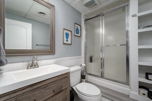 Een badkamer met een wit wastafel, houten wastafelmeubel, toilet en douchecabine met glazen wanden.