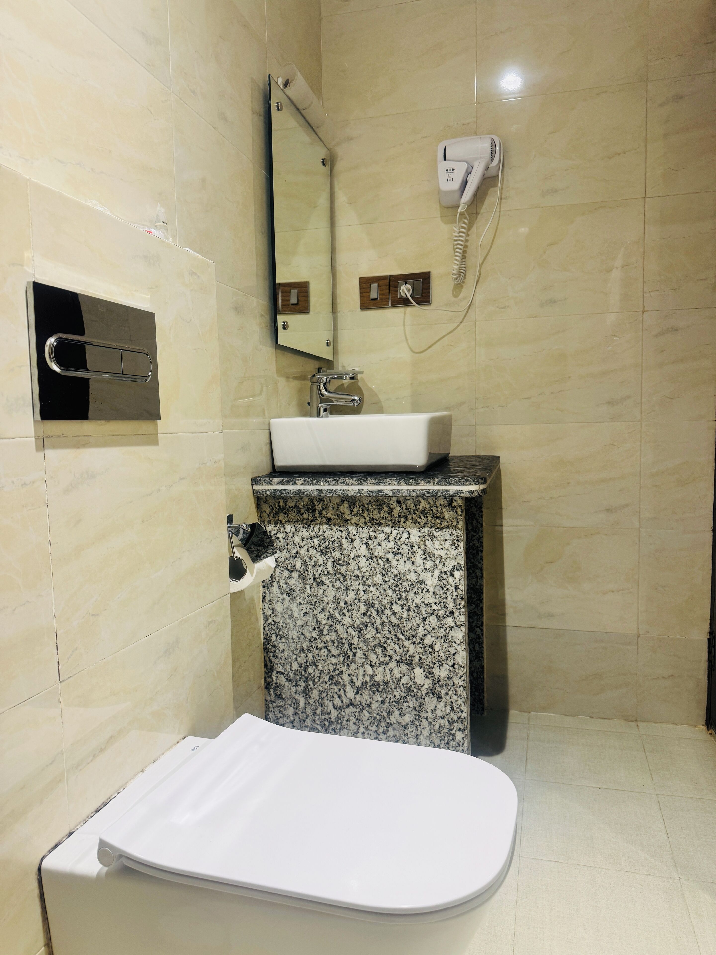 Ein Badezimmer mit einer weißen Toilette, einem Waschbecken mit Granitplatte, einem Spiegel und einem an der Wand befestigten Fön.