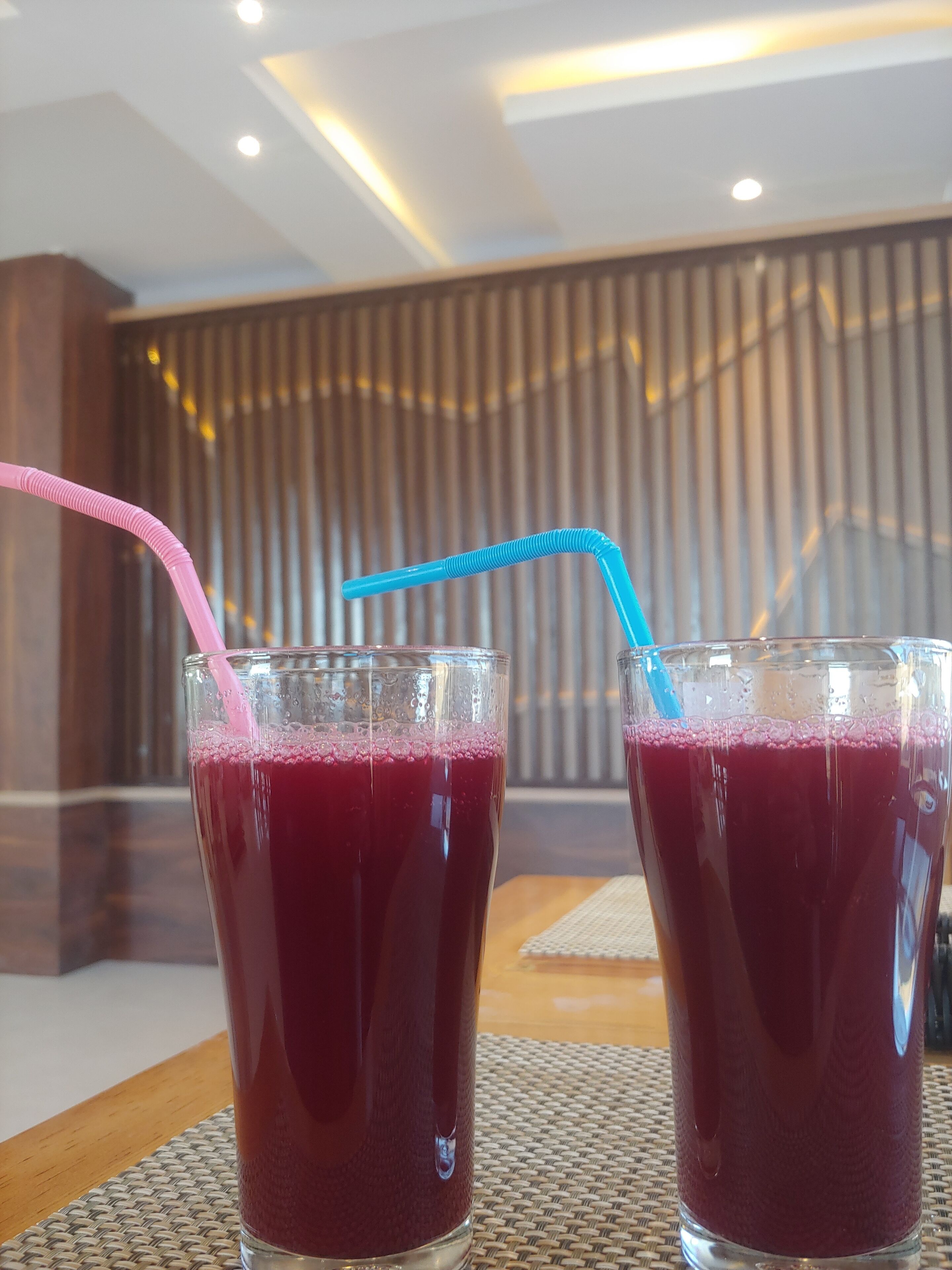 Deux verres d’une boisson rouge, chacun muni d’une paille, sont posés sur une table dans une pièce au décor moderne.