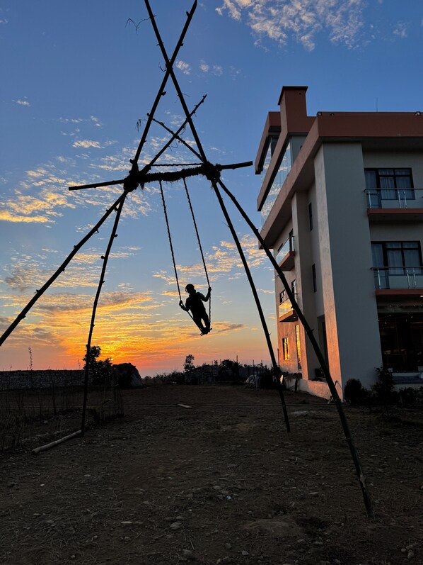 A swing set in a rural setting with a modern building in the background.