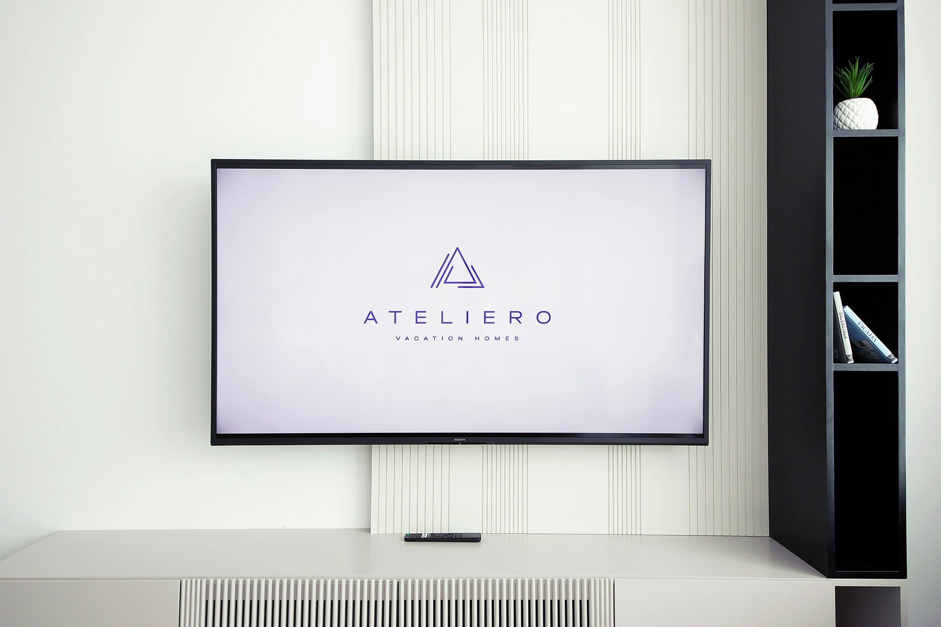 A flat-screen TV mounted on a wall with a logo reading "ATELIERO Vacation Homes."