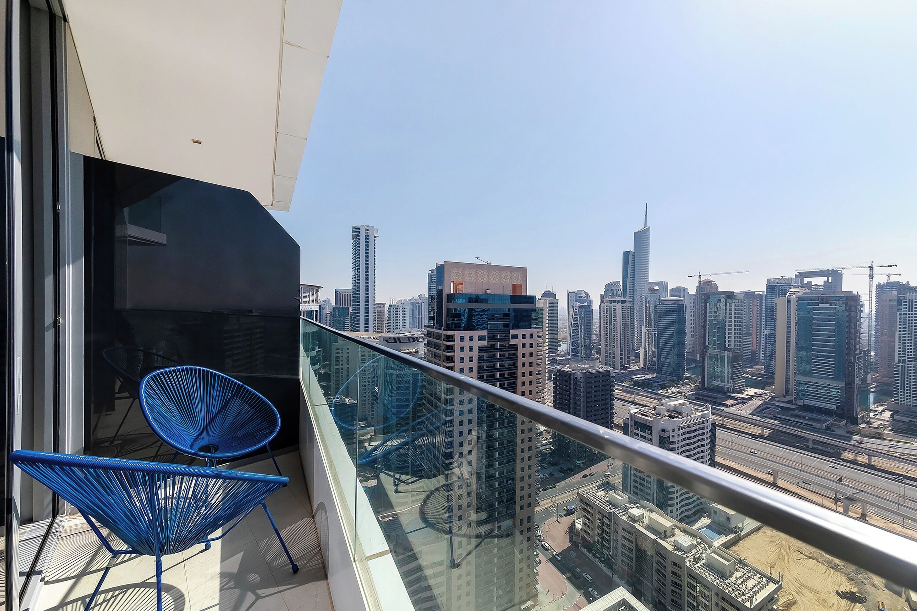 A balcony with a glass railing overlooking a cityscape with high-rise buildings and construction cranes.