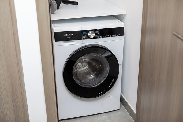Una lavadora blanca de Siemens en una esquina de una habitación con suelo de madera y una puerta.