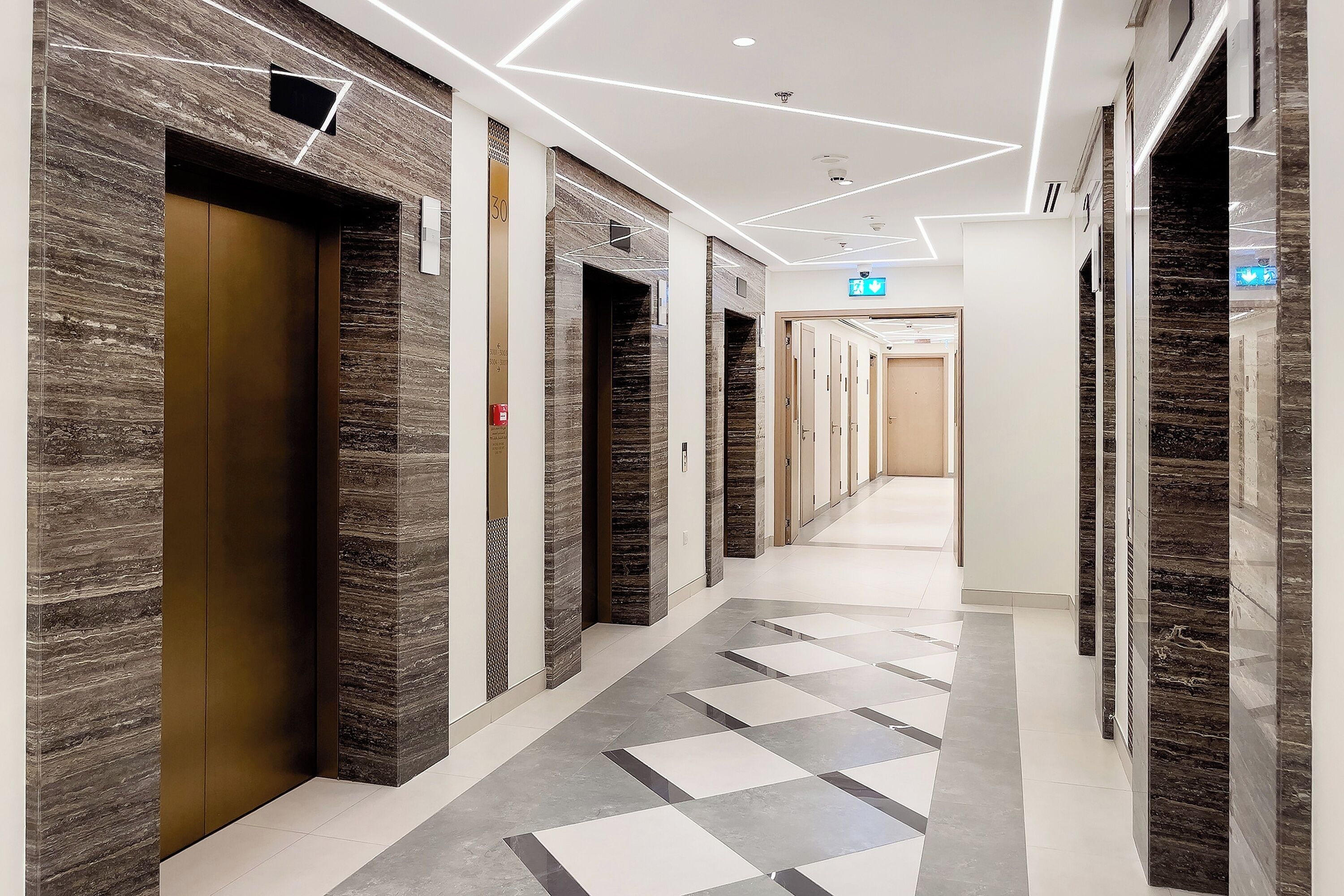 Un pasillo moderno de hotel con paredes de mármol, piso a cuadros y varias puertas.
