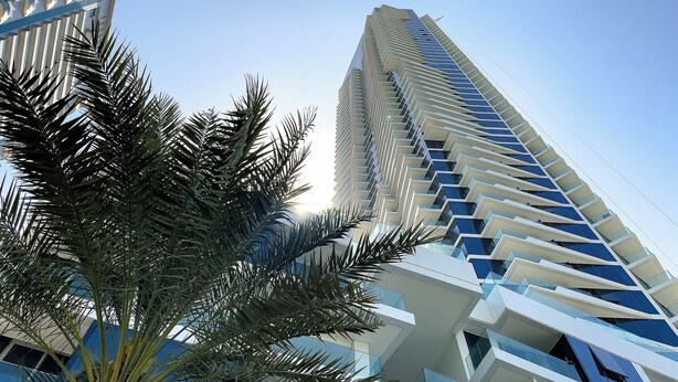 A modern high-rise building with a unique zigzag facade and a palm tree in the foreground. - Stella Maris Tower (Dubai)