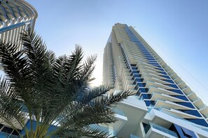 Un moderno edificio de gran altura con una fachada en zigzag distintiva y una palmera en primer plano.