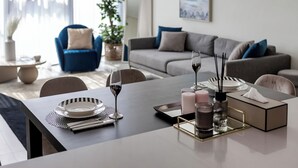 A modern dining area with a table set for two, featuring a white tablecloth, plates, cutlery, glasses, candles, and a tissue box. - Stella Maris Tower (Dubai)