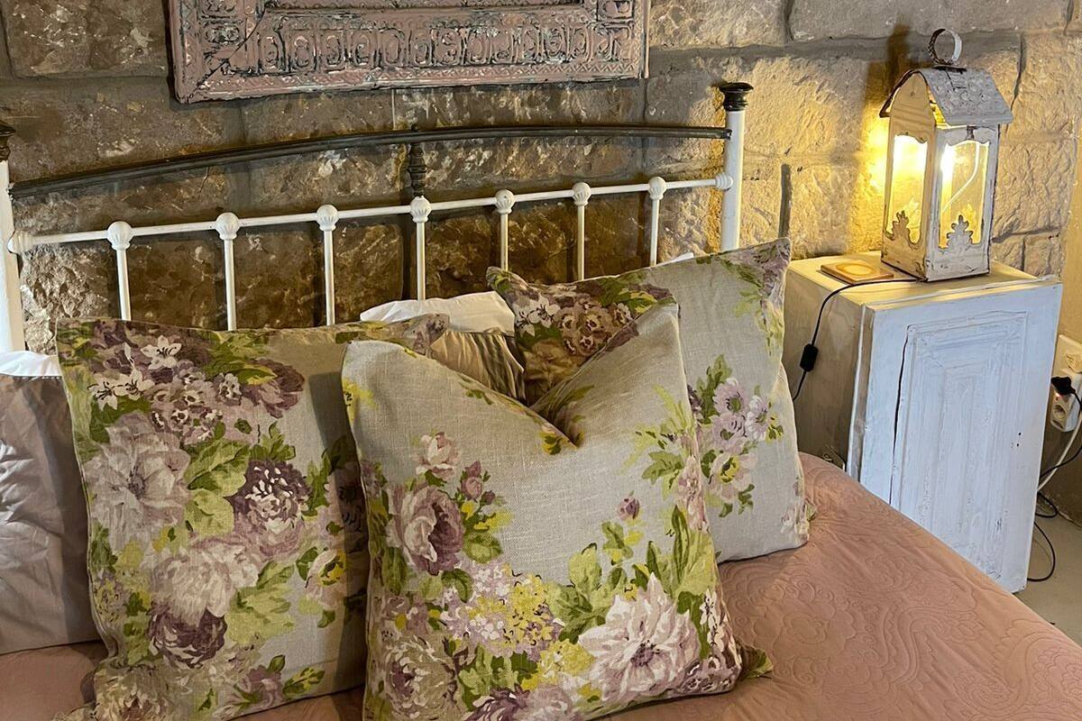 Ein Bett mit blumigen Kissen, eine Steinsäule und ein gerahmtes Bild darüber.