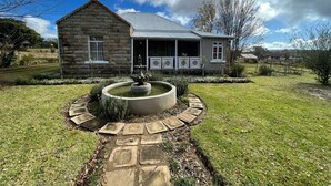 Una casa de piedra con un porche y una fuente en el jardín.