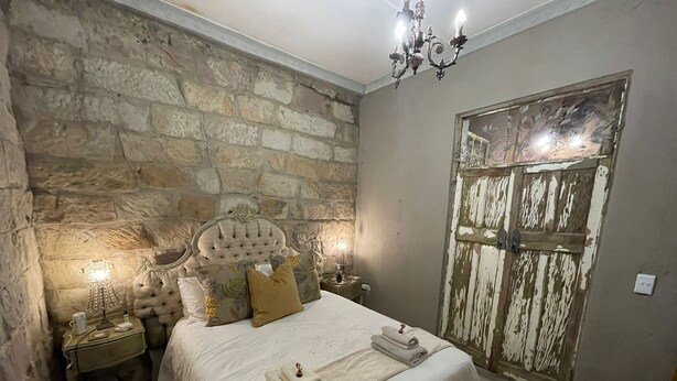 Un dormitorio con pared de piedra, cabecera capitonada, una puerta de madera grande y un candelabro.