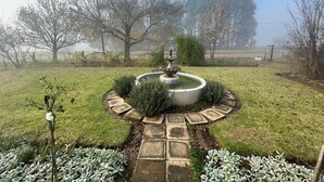 Un jardín con una fuente, un sendero de piedra y diversas plantas.