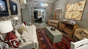 Una sala de estar acogedora con pared de piedra, un sofá blanco, un tapete estampado y un cuadro abstracto de gran tamaño.