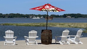 Una playa con sillas Adirondack blancas y una sombrilla roja de estampado cuadriculado.