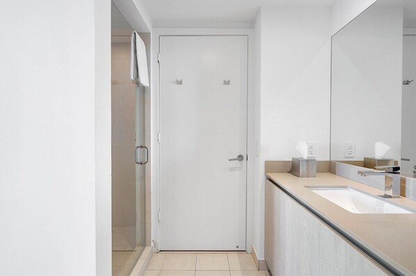 A modern bathroom with a white door, a glass shower enclosure, a sink with a mirror, and a towel rack.
