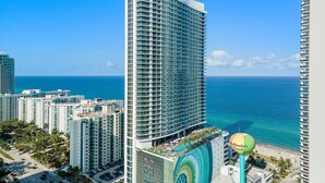 A high-rise hotel with a curved facade, multiple balconies, and a view of the ocean.