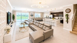 A modern living room with a sectional sofa, a dining area, a kitchen, and a staircase.