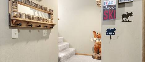 Un escalier sur lequel se trouve une étagère en bois, où sont disposés divers objets. On peut également voir des décorations murales, dont une enseigne indiquant « Bienvenue dans notre chalet » et une autre qui dit « Paix, amour et ski ».