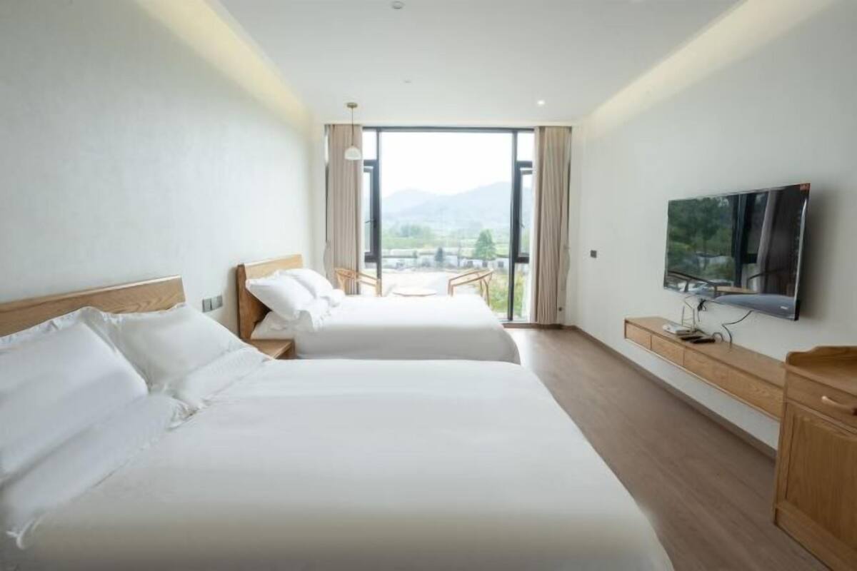 Habitación de hotel con dos camas, televisión y balcón con vistas.