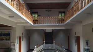 Un amplio atrio con una escalera central, barandillas de madera y una fuente decorativa.