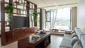 Ein modernes Wohnzimmer mit Fernseher, Holzschrank, Sofa und großen Fenstern.