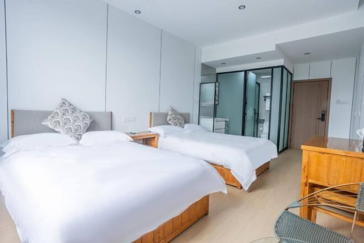 Una habitación de hotel moderna con dos camas, un escritorio de madera y un separador de vidrio.