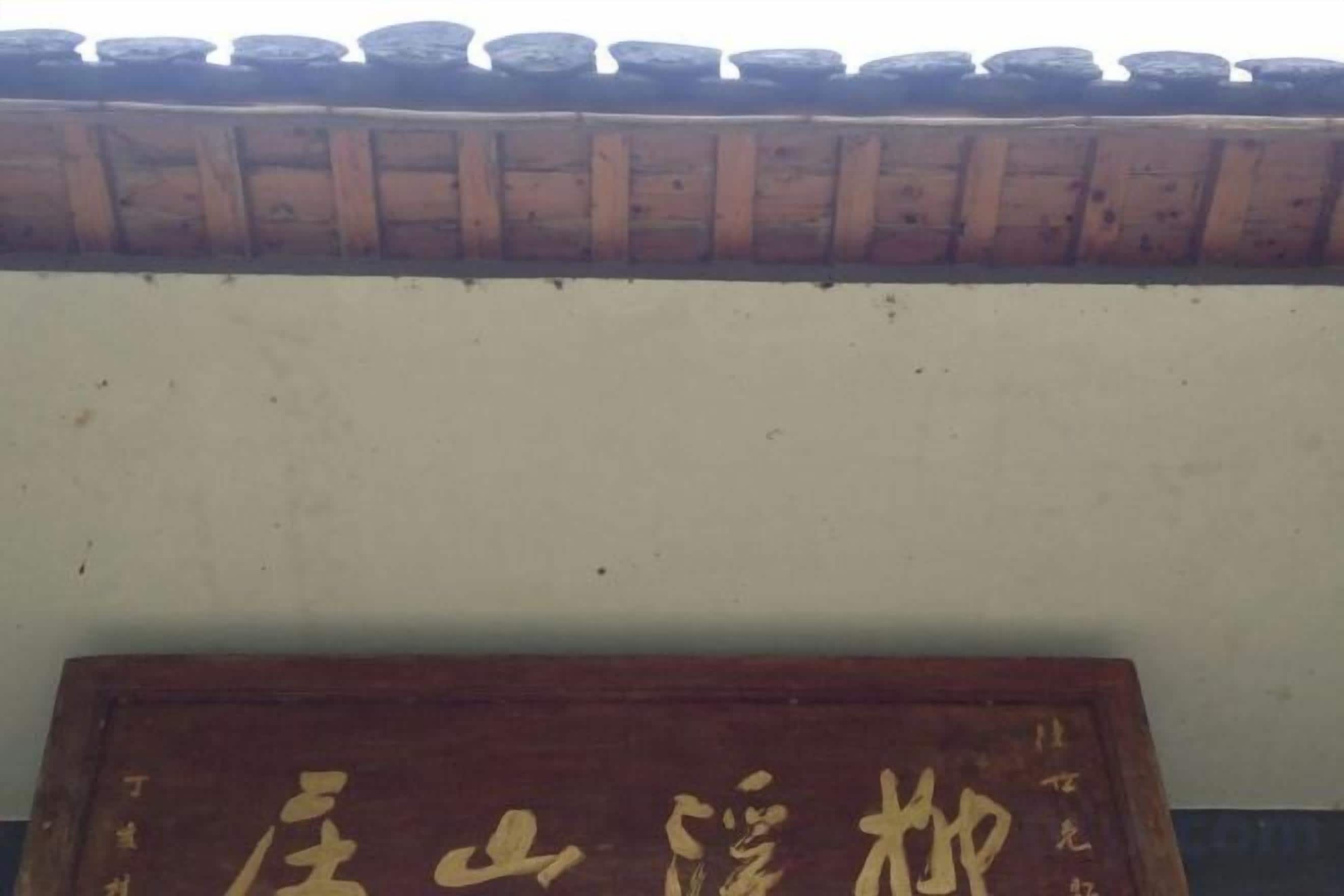 A wooden sign with characters, a tiled roof, and a plain wall.