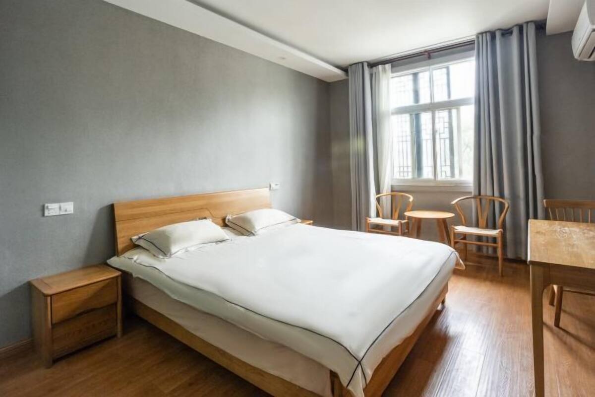 Un dormitorio con una cama de madera, una mesita de noche, una pequeña mesa, dos sillas y una ventana con cortinas.