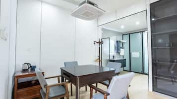 A modern meeting room with a dark wooden table, four chairs, a small wooden side table with a kettle, and a ceiling-mounted air purifier.