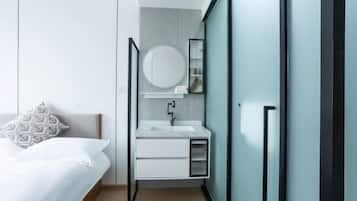 A modern bedroom with a bed, a bedside table, a round mirror, and a built-in white cabinet with a sink.