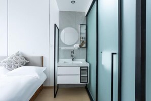 Ein modernes Schlafzimmer mit Bett, Nachttisch, rundem Spiegel und integriertem weißem Schrank mit Waschbecken.