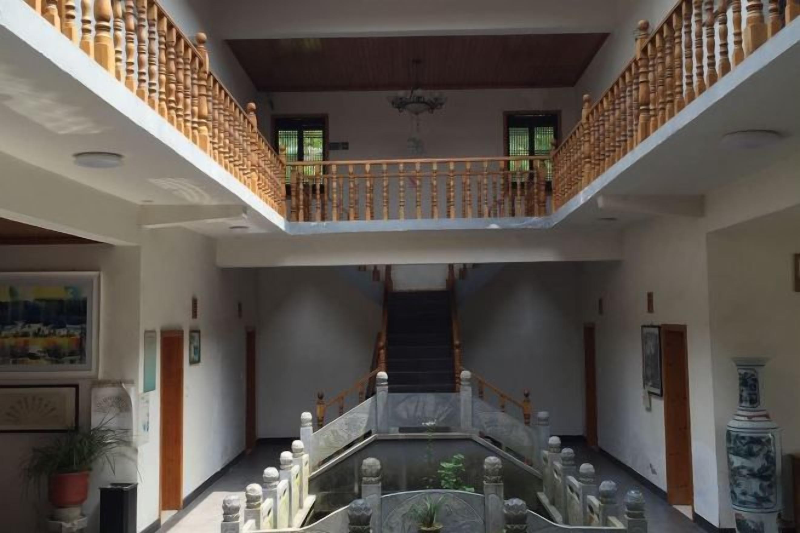 Un interior de diversos nivells amb una escala central, baranes de fusta i una font decorativa.