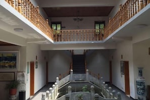 A multi-level interior with a central staircase, wooden railings, and a decorative fountain. - Liuxi Hostel (Jing County)