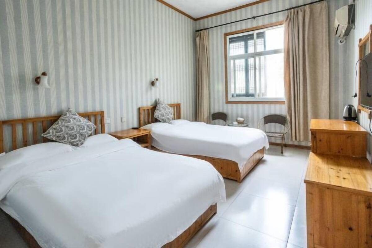 Habitación de hotel con dos camas, un escritorio, una silla y una ventana con cortinas.