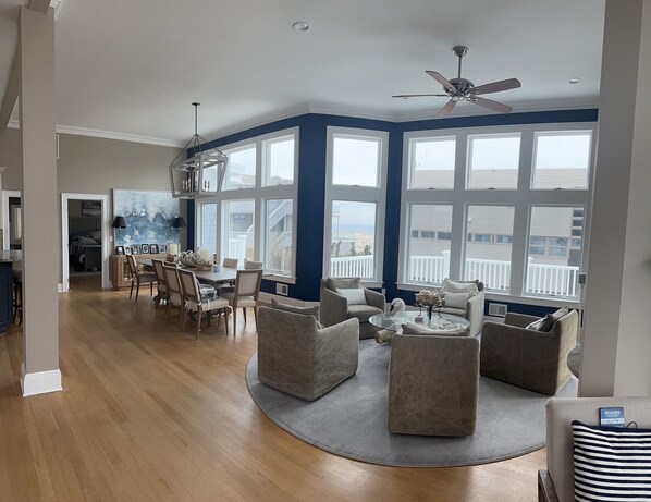 Relax in this spacious living area with a high ceiling and ceiling fan, featuring large windows with an outside view.