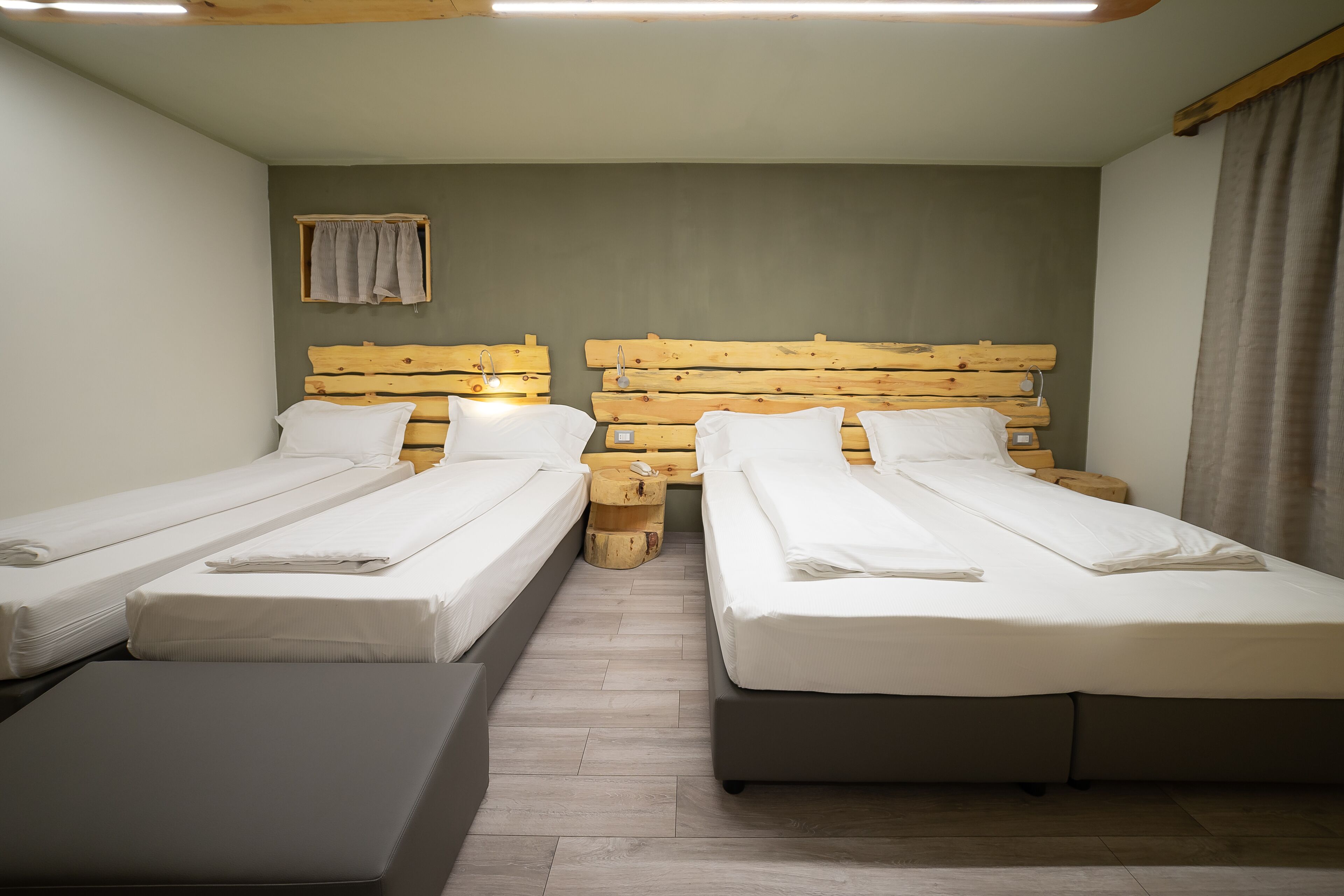 A room with two single beds, a small window with a curtain, and a wooden headboard.