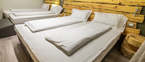 A room with three single beds, wooden headboards, and a wooden floor.