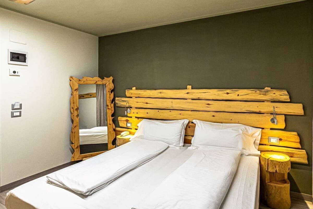 Un lit double avec une tête de lit en bois, une table de chevet, un miroir et une lampe de chevet.