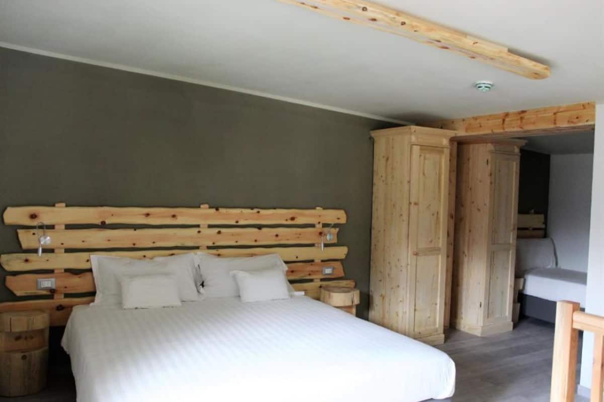 Une chambre à coucher avec une tête de lit en bois, un lit avec une literie blanche, une armoire en bois et un petit tabouret en bois.