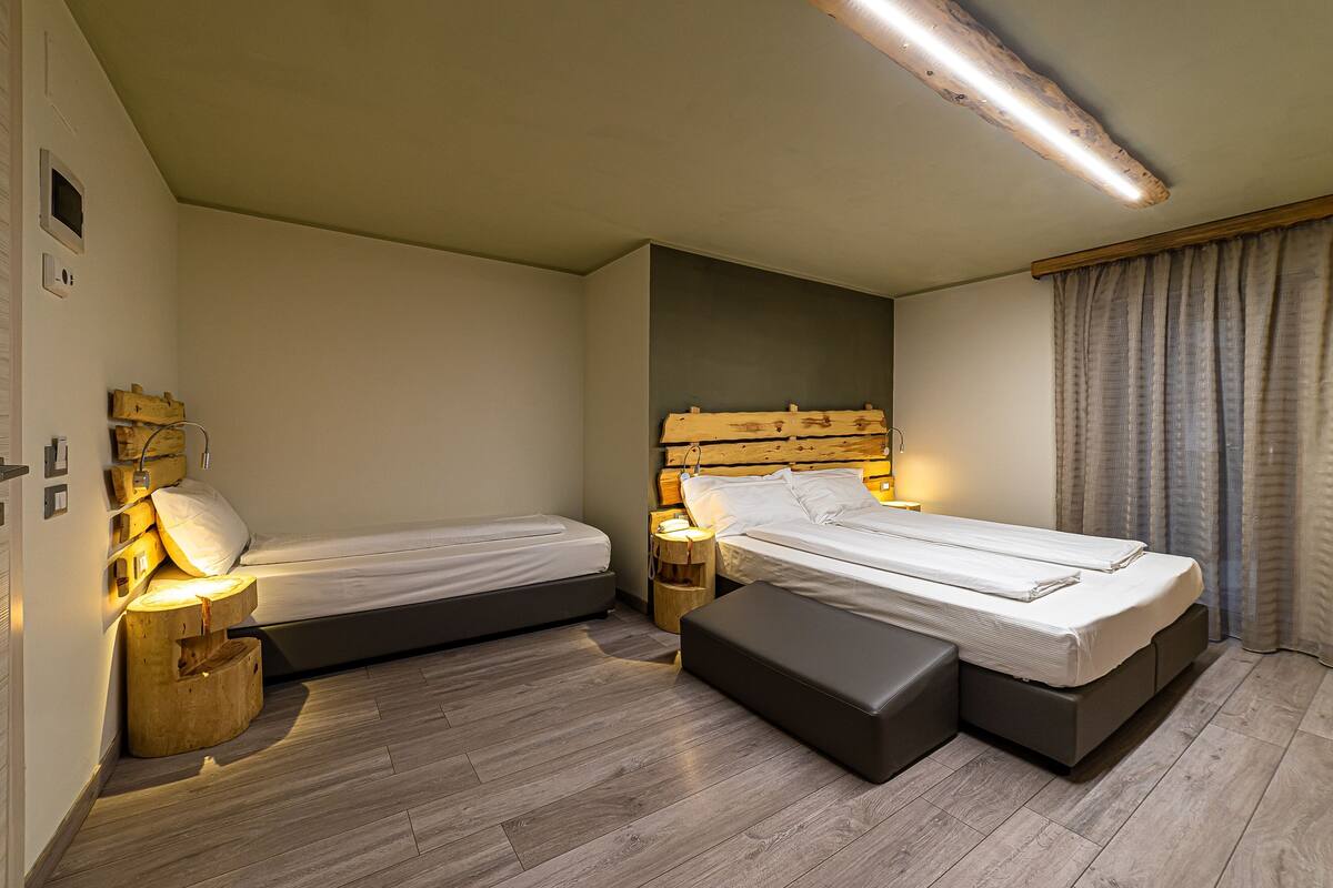 Une chambre avec deux lits simples, un banc, une tête de lit en bois, des tables de chevet avec des lampes et un plancher en bois.