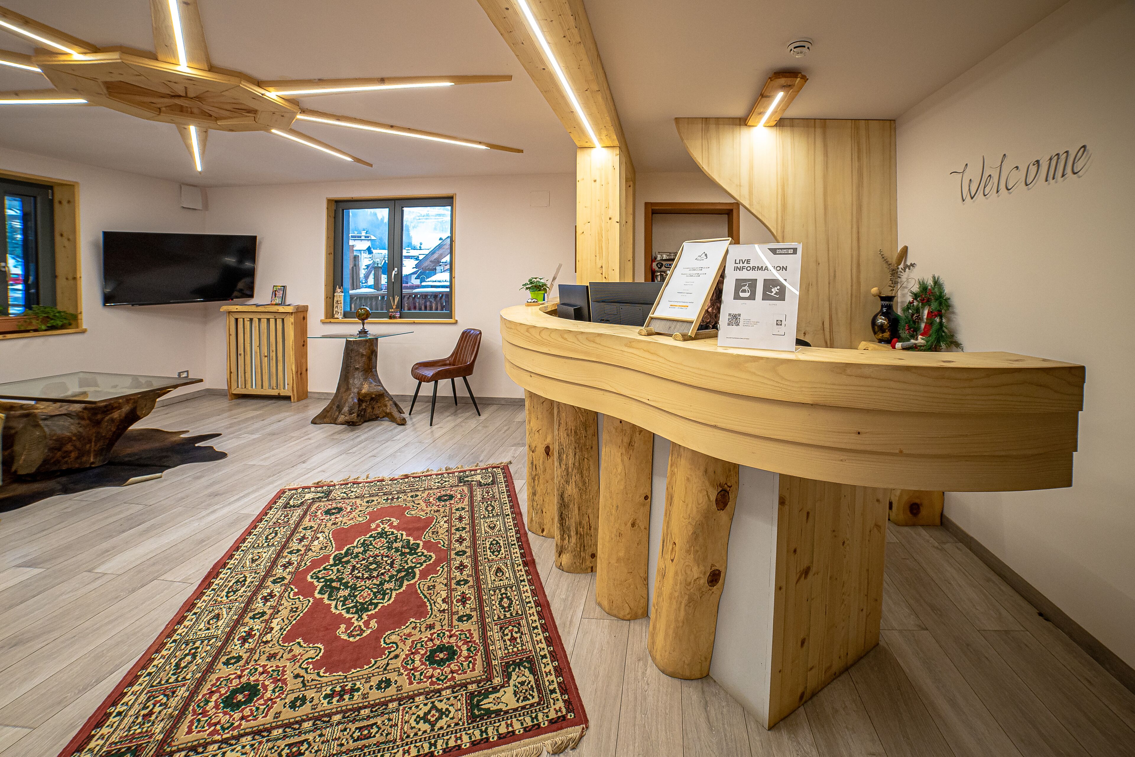 Een receptiebalie met een 'Welcome'-bord, een houten balie, een grote flatscreen-televisie, een tapijt met patroon en een houten vloer.