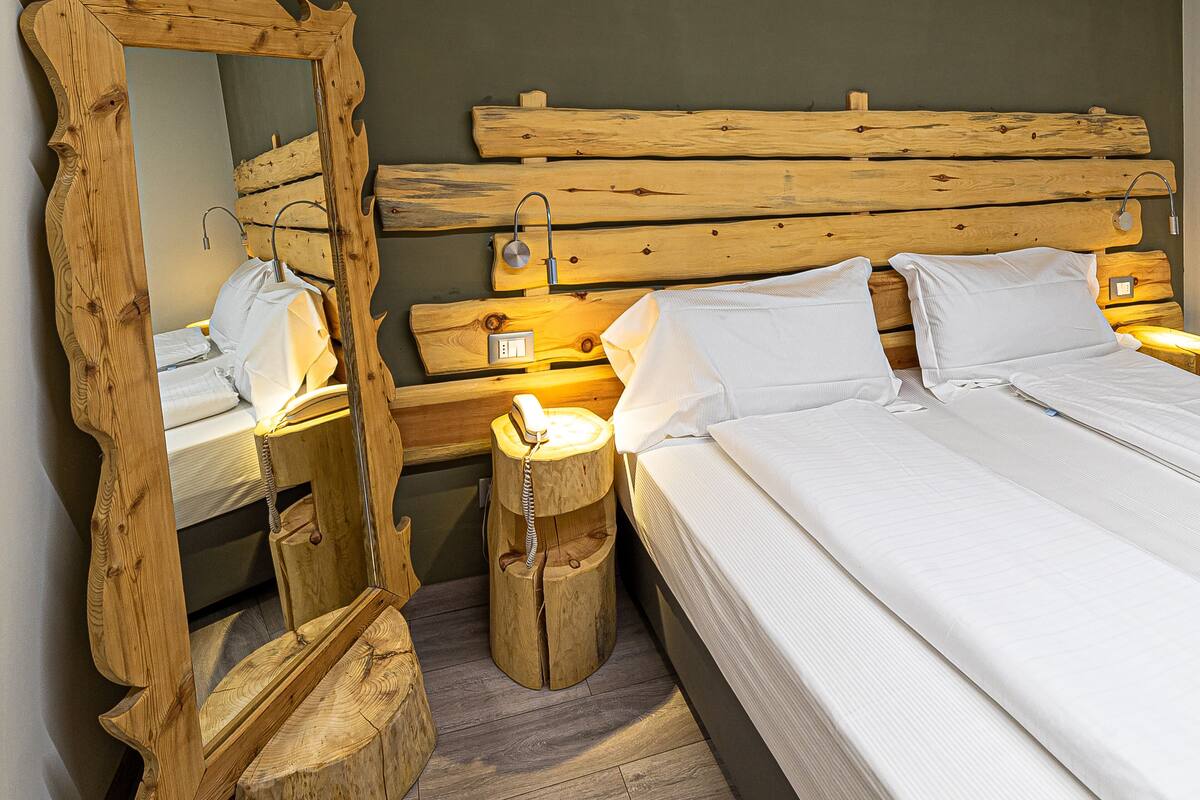 Une chambre à coucher avec une tête de lit en bois, un grand miroir, une table de chevet et un lit avec une literie blanche.