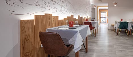 A dining area with wooden partitions, tables with white tablecloths, and chairs.