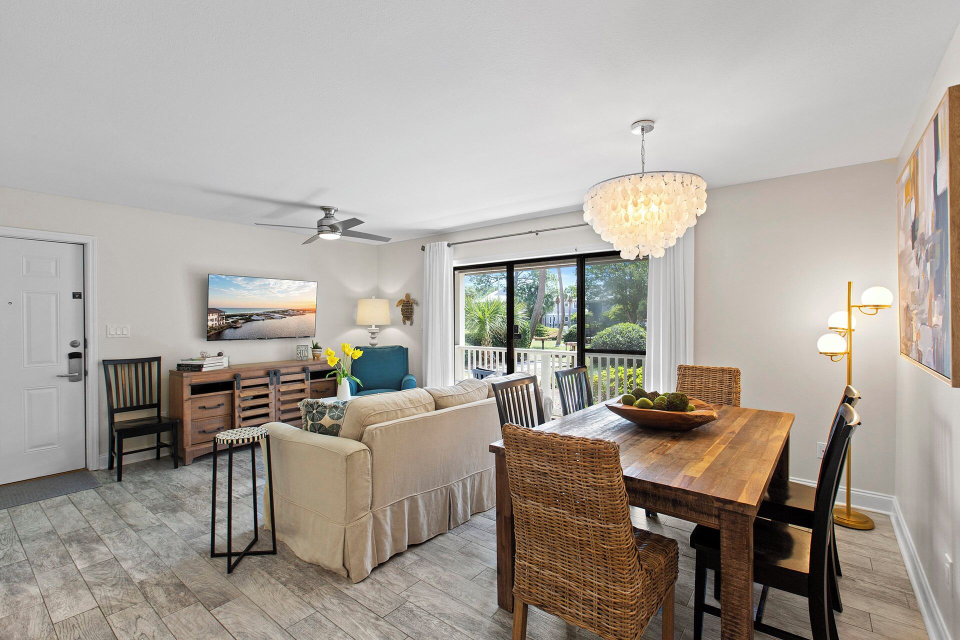 A spacious living area with a sofa, dining table, and chairs, a ceiling fan, and a view of the outdoors.