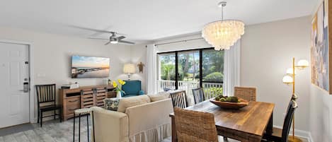 A spacious living area with a sofa, dining table, and chairs, a ceiling fan, and a view of the outdoors.