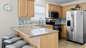 Une cuisine moderne avec des meubles en bois, des appareils en acier inoxydable, un plan de travail en granit et un îlot central intégré avec des tabourets de bar.